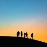 Silhouettes of adventurers on sand dunes against a vibrant sunset sky in the Sahara Desert.